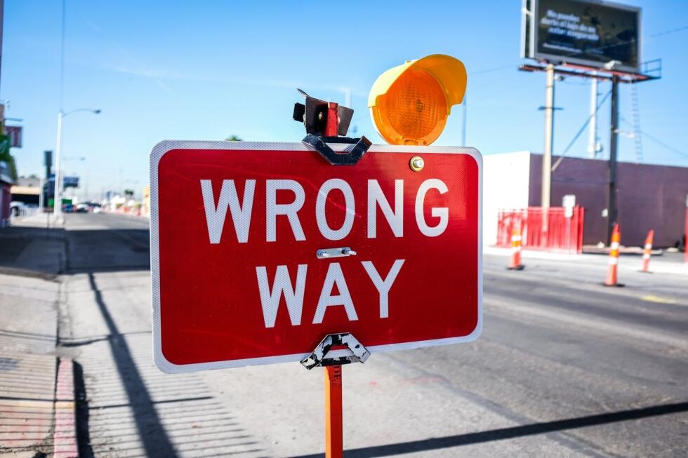 Czerwona tablica ostrzegawca z napisem "Wrong way" stojąca na drodze. Unsplash: Quilia