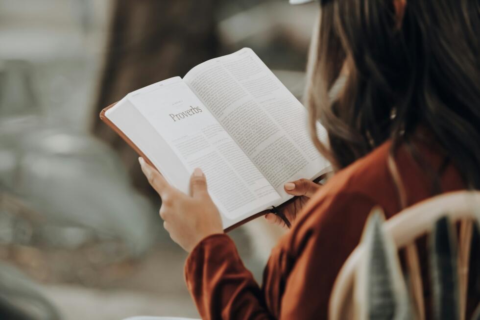Kobieta trzyma w dłoniach i czyta książę, którą ma otwartą na rozdziale "Proverbs".