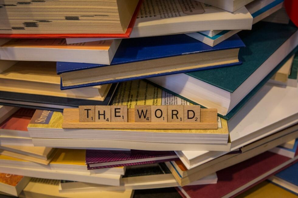 Słowo "The word" ułożone z liter z gry Scrabble na stosie książek. Unsplash: Mick Haupt
